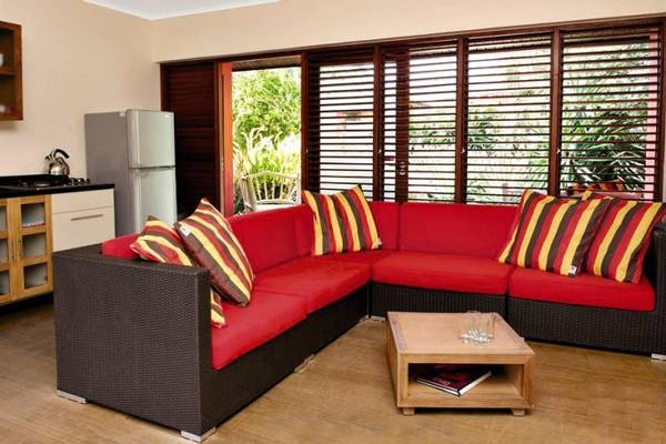 Innenbereich des Morena Eco Resorts mit einer roten Eckcouch, Kissen und einem Tisch vor einer offenen Tür.