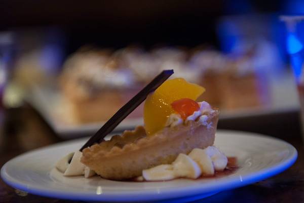 Dessertplatte mit einer Tarte, die mit Sahne, Früchten und Schokoladendutteln verziert ist.