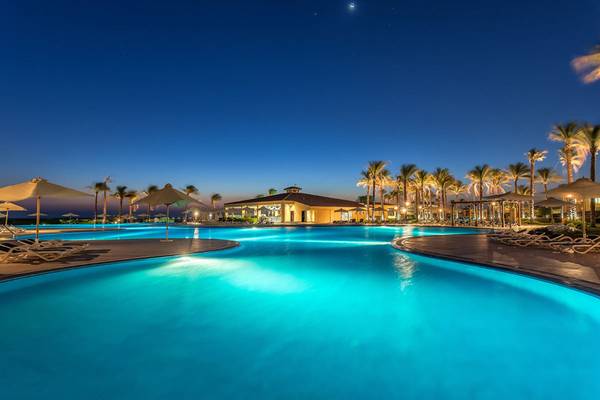 Poollandschaft im Cleopatra Luxury Beach Resort bei Nacht mit beleuchteten Palmen und Sonnenschirmen.