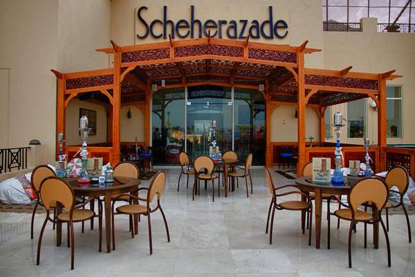 Außenbereich des Scheherazade Hotels mit runden Tischen und Stühlen unter einem hölzernen Baldachin.