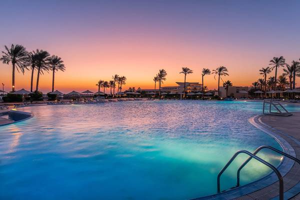 Pool im Cleopatra Luxury Beach Resort bei Sonnenuntergang mit Palmen und Hotelgebäude im Hintergrund