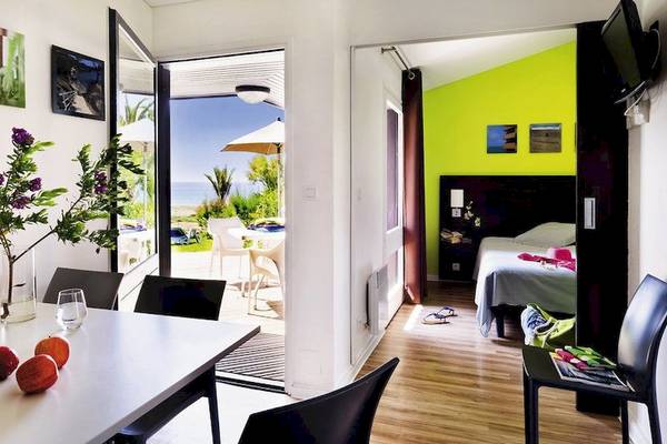 Innenansicht des Belambra Club Golfe de Lozari Hotels mit Wohnbereich, Esstisch und Blick auf die Terrasse.