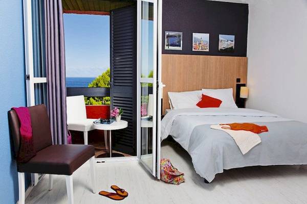Hotelzimmer mit Balkon und Meerblick, Bett, Tisch, Stühle und offene Tür.