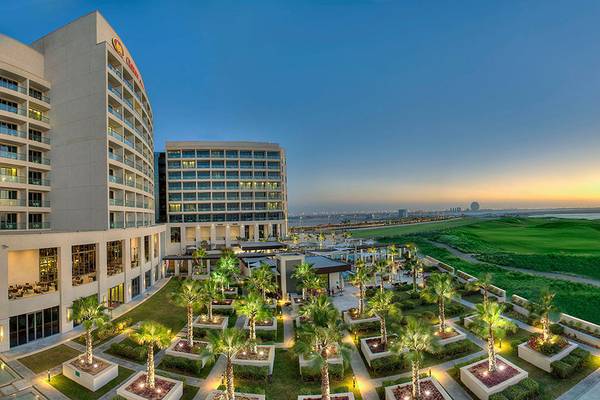 Außenansicht des Crowne Plaza Abu Dhabi Yas Island Hotels mit angelegtem Golfplatz und illuminierten Palmen im Vordergrund.