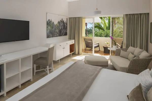 Innenansicht eines Zimmers im Melia Caribe Beach Resort mit einem Bett, Schreibtisch, Fernseher, Minibar und Balkon.