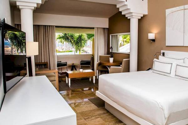 Innenansicht eines eleganten Zimmers im Melia Caribe Beach Resort mit einem großen Bett, Fernseher, Schreibtisch und Aussicht auf Palmen.