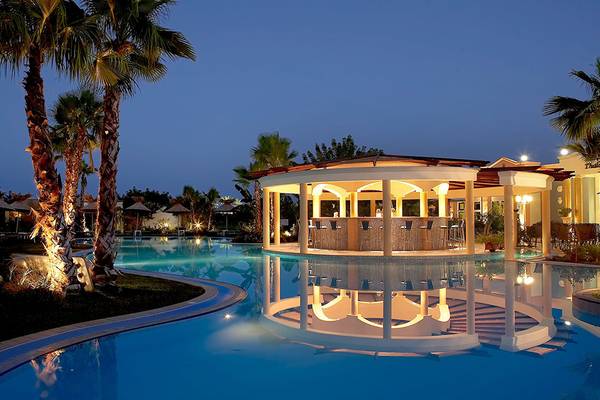 Nachtansicht des Swimmingpool-Bereichs des Atrium Palace Thalasso Spa Resort & Villas mit Palmen und einer Bar.