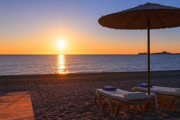 Sonnenuntergang am Strand mit zwei Sonnenliegen und einem Sonnenschirm