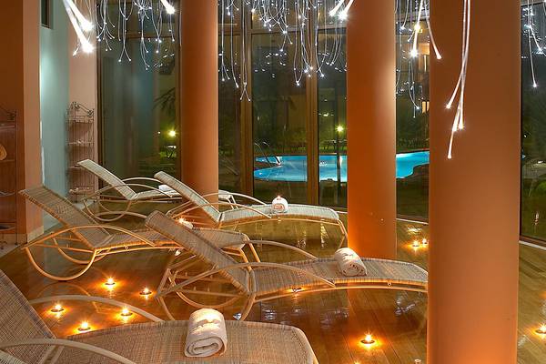 Innenbereich des Atrium Palace Thalasso Spa Resorts mit Lounge-Liegestühlen, Beleuchtung und Blick auf den Pool.