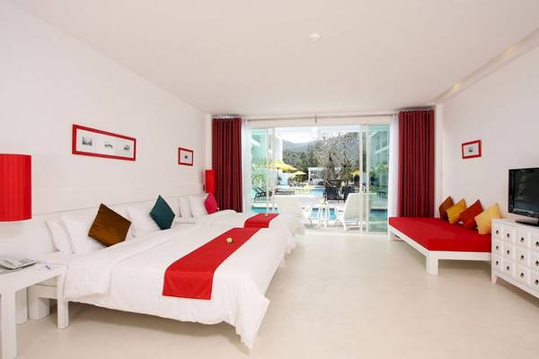 Hotelzimmer im The Old Phuket - Karon Beach Resort mit zwei Betten, rotem Vorhang und Poolblick.