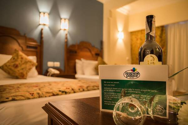 Ein Bett im Jasmine Palace Resort & Spa mit einer Flasche Wein und leeren Gläsern auf einem Nachttisch.