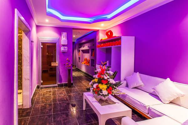 Innenbereich des Jasmine Palace Resort & Spa mit lila Wänden, einem weißen Sofa, einer Tisch mit Blumen und einer Saunatür.