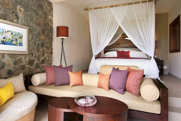 Innenansicht des Schlafzimmers im Kempinski Seychelles Resort mit Bett, Couch, Lampen und Gemälde.