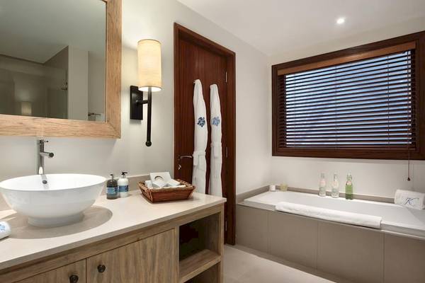 Badezimmer im Kempinski Seychelles Resort mit Waschbecken, Spiegel, Badewanne und Fenstern.