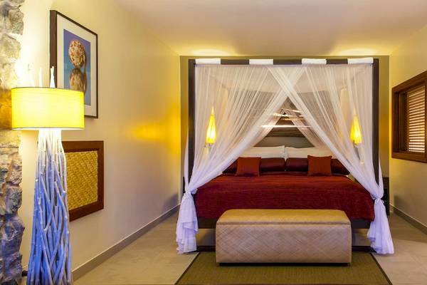 Schlafzimmer im Kempinski Seychelles Resort mit einem großen Bett, roter Bettwäsche und weißen Vorhängen, umgeben von gelben Wänden.