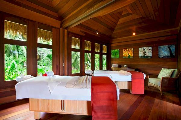 Zwei Betten im Holzraum des Kempinski Seychelles Resort mit Blick auf grüne Pflanzen und Fenstern.