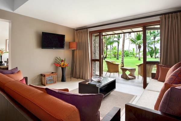 Wohnbereich des Kempinski Seychelles Resort mit Fernseher, Sofas und Glastür zum Garten.