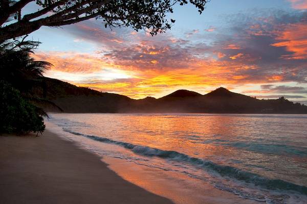 Sonnenuntergang am Strand des Kempinski Seychelles Resort mit leuchtenden Farben und sanften Wellen