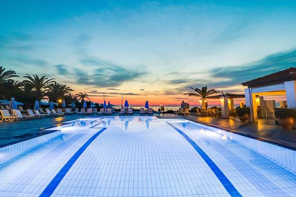 Außenpool des Creta Royal Hotels bei Sonnenuntergang, umgeben von Lounge-Stühlen und Palmen.