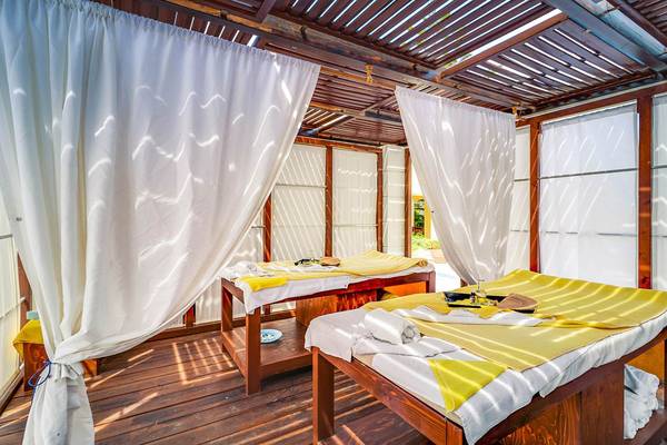 Spa-Behandlungsraum im Creta Royal Hotel mit zwei Behandlungstischen, gelben Decken und weißen Vorhängen.