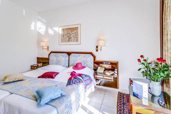Innenansicht eines Zimmers im Creta Royal Hotel mit einem Doppelbett, einem Nachttisch und einer Vase mit Blumen.