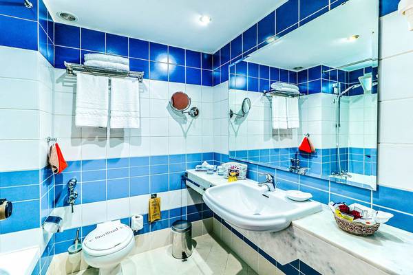 Badezimmer des Creta Royal Hotels mit blauen und weißen Fliesen, Toilette, Waschbecken und Spiegel.