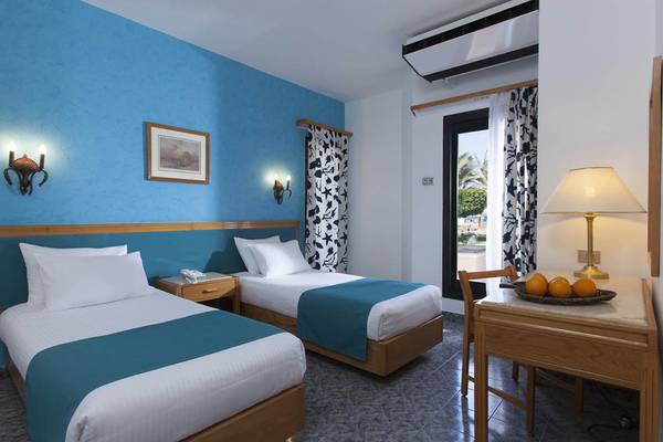 Zweibettzimmer im Pharaoh Azur Resort mit blauen Wänden, zwei Betten, Nachttischen, Lampen und einem Tisch mit Früchten.