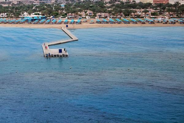 Luftaufnahme des Strandes am Pharaoh Azur Resort mit blauen Sonnenschirmen und einem Steg im Wasser.