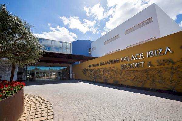 Eingang des Grand Palladium Palace Ibiza Resort & Spa mit gelber Wand und rot blühenden Pflanzen