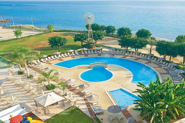 Luftaufnahme des Pernera Beach Hotels mit Swimmingpool, Sonnenliegen, Bäumen und Meer im Hintergrund.