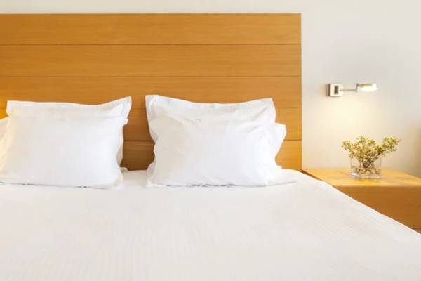 Bett im Alion Beach Hotel mit weißen Laken und Kissen auf einem weißen Kopfteil.