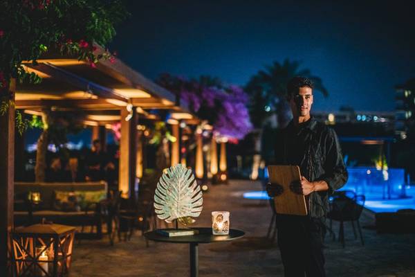 Mann im Alion Beach Hotel Außenbereich bei Nacht, mit Tisch und Poolbeleuchtung im Hintergrund.
