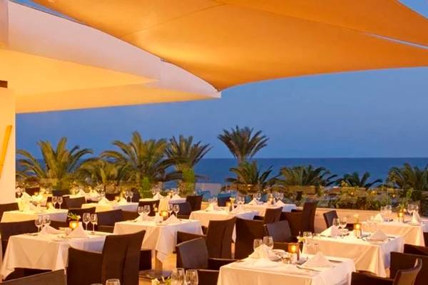 Außenbereich des Alion Beach Hotels mit Blick auf das Meer und Palmen bei Sonnenuntergang.