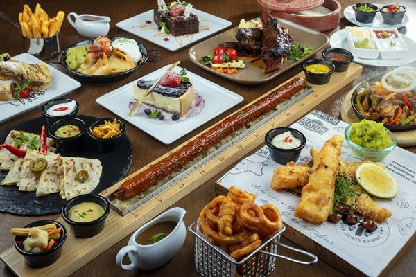 Vielfalt an Gerichten auf Holztisch, darunter Burger, Quesadillas, Desserts und Dips.