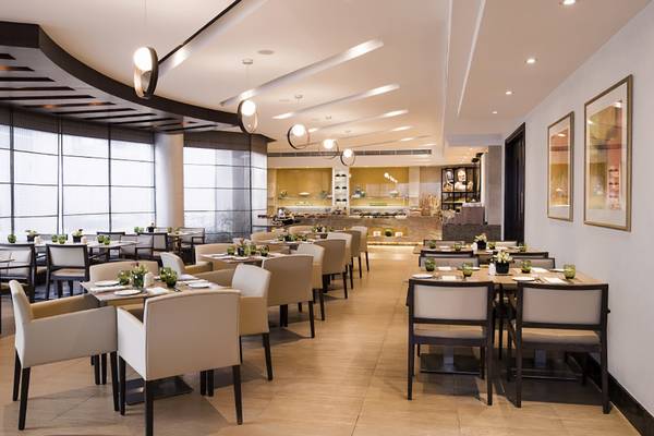 Innenansicht des Restaurants im Jumeira Rotana Hotel mit gepolsterten Stühlen und Tischen.