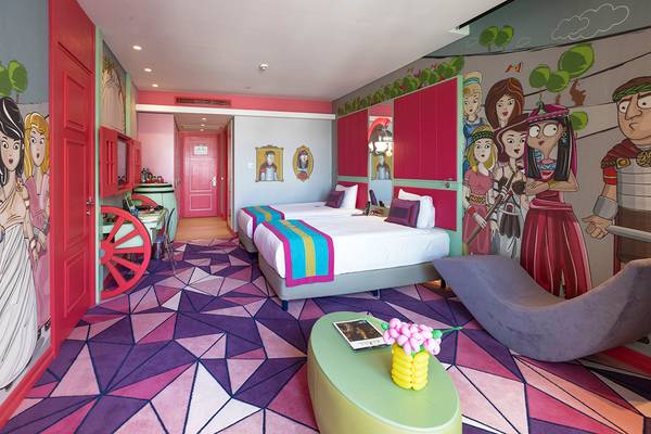 Hotelzimmer im Land der Legenden Königreich mit farbenfrohen Wänden, zwei Betten und geometrischem Teppich.