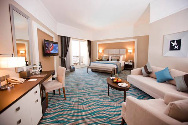 Luxuriöses Hotelzimmer im Rixos Bab Al Bahr mit Kingsize-Bett, Wohnzimmerbereich und moderner Einrichtung.