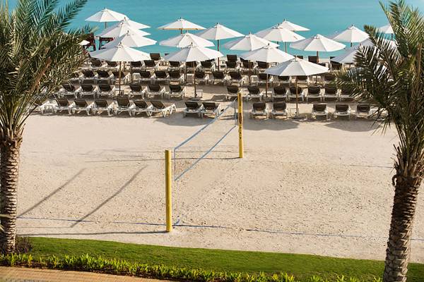 Strand mit Volleyballnetz und vielen Sonnenschirmen und Liegen am Rixos Bab Al Bahr Hotel.