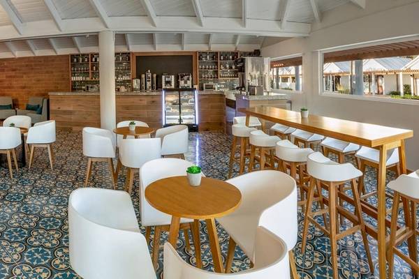 Innenansicht des Grand Sirenis Punta Cana Resorts mit Loungebereich, Bar, Tischen und Stühlen.