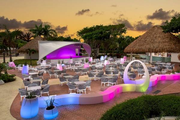 Außenbereich des Grand Sirenis Punta Cana Resorts bei Abend mit farbigen Beleuchtung und Tischen und Stühlen.
