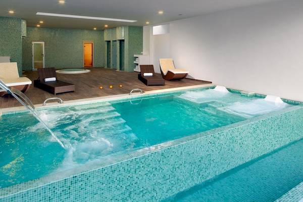 Ein Indoor-Schwimmbecken im Grand Sirenis Punta Cana Resort mit Wasserfall und Liegestühlen.