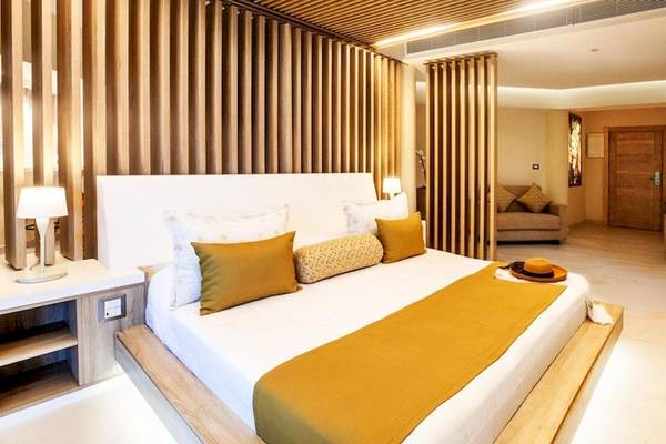 Innenansicht eines Hotelzimmers im Grand Sirenis Punta Cana Resort mit einem großen Bett, Holzwänden und Möbeln.