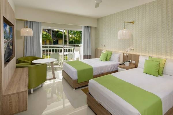 Doppelzimmer im Grand Sirenis Punta Cana Resort mit zwei Betten, grünen Kissen und einem Balkon.