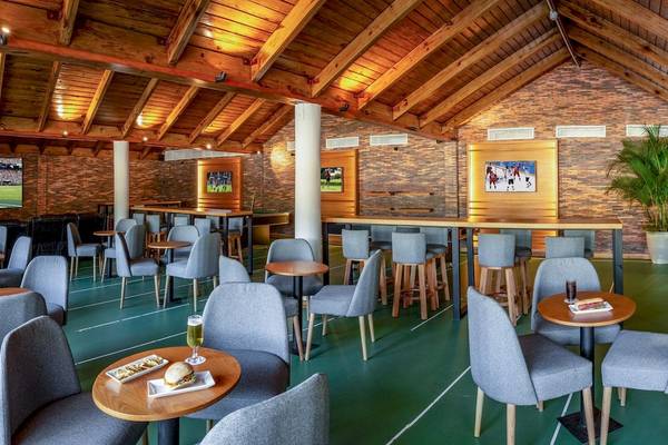 Innenbereich des Grand Sirenis Punta Cana Resort mit mehreren Tischen und Stühlen, Fernsehern an der Wand und einer grünen Spielfläche.