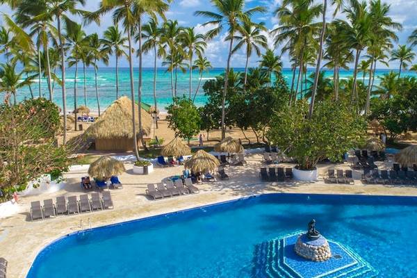 Außenbereich des Grand Sirenis Punta Cana Resorts mit Swimmingpool und Sonnenliegen am Strand