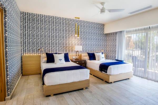 Zwei Betten im Hotelzimmer des Grand Sirenis Punta Cana Resort mit blauen und weißen Decken und Kissen.