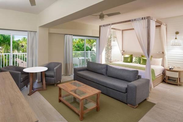Innenansicht einer Suite im Grand Sirenis Punta Cana Resort mit Wohnzimmer und Schlafzimmerbereich.