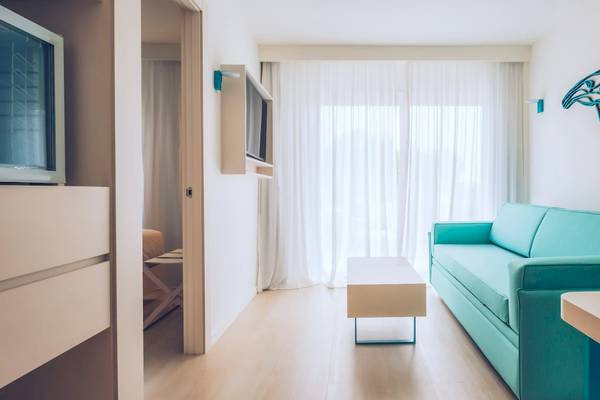 Ein modernes Hotelzimmer im Iberostar Waves Alcudia Park mit einer blauen Couch, einem Couchtisch und einem Fernseher.