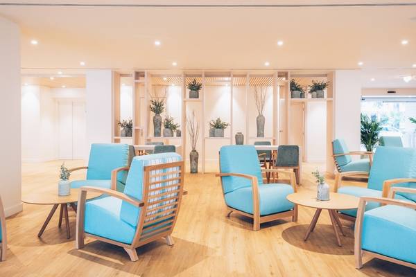 Hotellobby des Iberostar Waves Alcudia Park mit blauen Sesseln und Holzboden, umgeben von Pflanzen und modernen Möbeln.