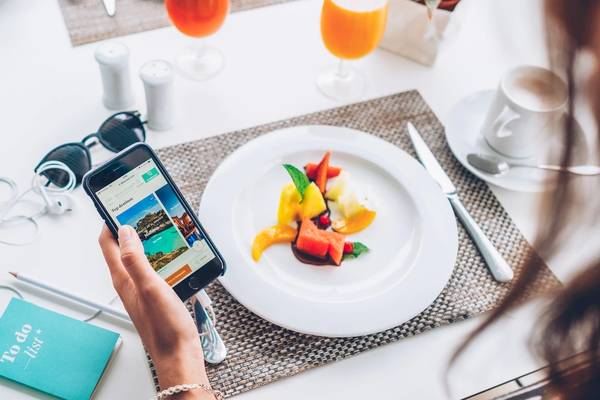 Eine Frau hält ein Smartphone mit der Website von Iberostar Waves Alcudia Park vor einem Frühstückstisch.